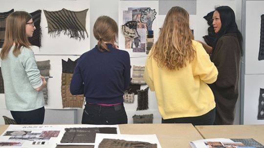 Four fashion design students looking at a wall with their work on